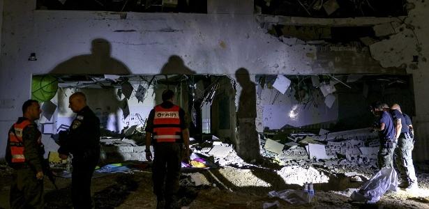 Membros do Comando da Frente Interna de Israel e forças policiais inspecionam uma cratera deixada por um projétil explodido em um prédio escolar na cidade de Gedera, no sul de Israel, depois que o Irã lançou mísseis contra Israel