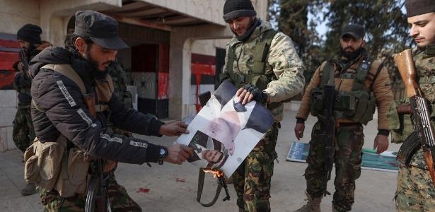 29.nov.2024 - Combatentes incendeiam uma foto do presidente sírio Bashar al-Assad em frente a um prédio tomado