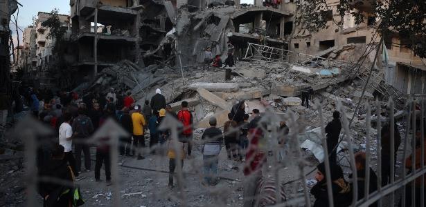 Palestinos ao lado dos escombros de um prédio após um ataque aéreo israelense ao refugiado de Nuseirat, no centro da Faixa de Gaza, em 13 de dezembro de 2024