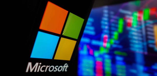 Logo da Microsoft em frente a painel com bolsa de valores