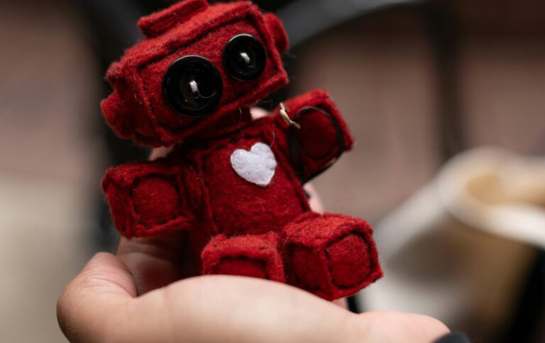 Mão segurando robô vermelho de inteligência artificial com coração