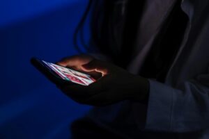Teenager looking at the cell phone in the dark, with the screen illuminating the face, in an image that represents the impact of fake news on young people.