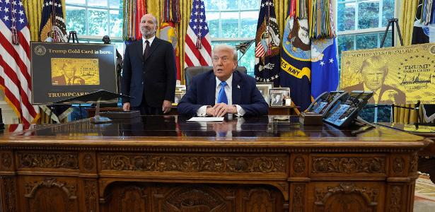 O presidente dos EUA, Donald Trump, fala sentado ao lado de uma placa que diz