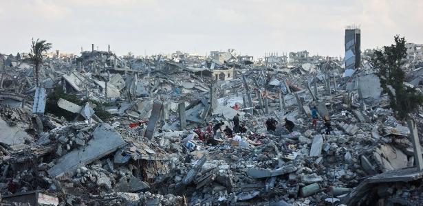 Palestinos vasculham escombros de prédios em meio à destruição generalizada causada pelos bombardeios israelenses em Khan Yunis, no sul da Faixa de Gaza