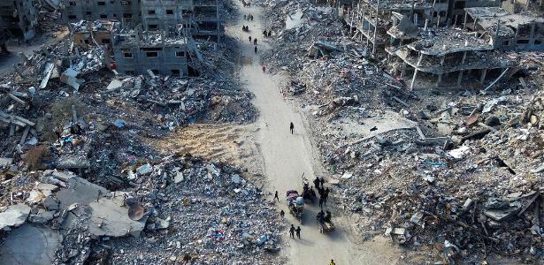 Foto aérea mostra pessoas atravessando estrada entre escombros em Rafah, no sul da Faixa de Gaza