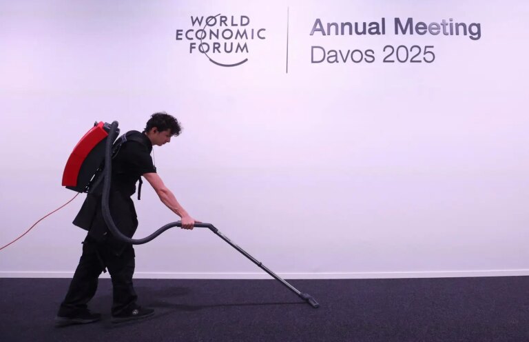 Um membro da equipe utiliza um aspirador de pó ao lado do logotipo do Fórum Econômico Mundial, antes do evento em Davos, Suíça, em 17 de janeiro de 2025. REUTERS/Yves Herman